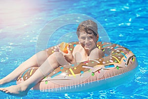 Happy cute little boy teenager lying on inflatable donut ring with orange in swimming pool. Active games on water, vacation