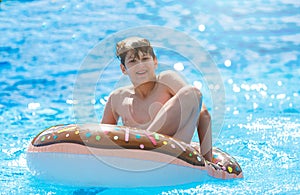 Happy cute little boy teenager lying on an inflatable donut ring in swimming pool. Active games on water, vacation, holidays