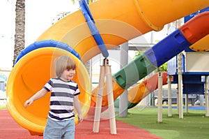 Happy cute little child boy having fun on a yellow slide outdoor in the park, sunny summer day in children playground.
