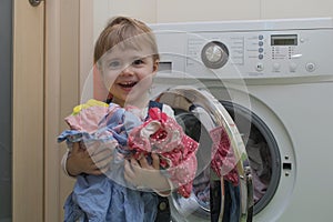 Happy cute little girl with clothes doing laundry in home interior