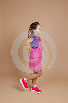 Happy cute little girl having yellow kanekalon braids, balancing on one leg with hands raised and put to sides looking
