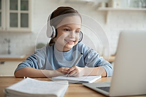 Happy cute little girl in headphones looking at laptop screen.