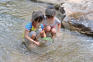 Happy cute little girl and her sister playing water in the stream. Little Asian sister enjoys swimming in the river. Healthy