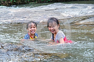 Happy cute little girl and her sister playing water in the stream. Little Asian sister enjoys swimming in the river. Healthy