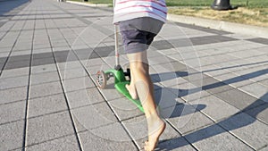 Happy cute little girl riding kick scooter in the park at sunny summer day