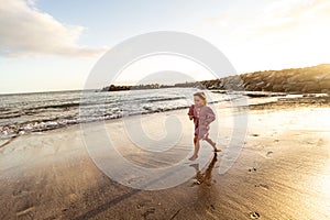 Happy cute little girl running in sand on beautiful beach during sunset. Summer holidays