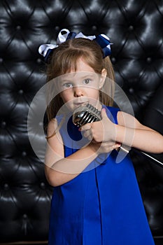 Happy Cute little girl singing a song on microphone. Black leathered background