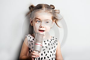 Happy Cute little girl singing a song on microphone. Grey background