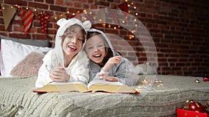 Happy Cute little kids are dressed in warm xmas pajamas laughs and looking at the camera, smiling children reads book at