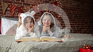 Happy Cute little kids are dressed in warm xmas pajamas laughs and looking at the camera, smiling children reads book at