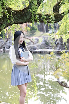 Happy cute lovely beautiful young girl high school college student enjoy free time read a book by a lake in summer park