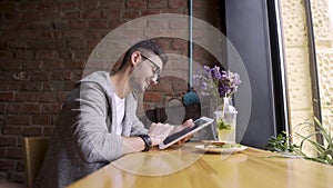 Happy cute male college student using tablet computer. guy sitting in a cafe with a tablet in her hands
