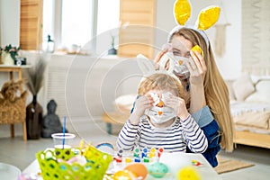 Happy cute mother and son wearing decorated bunny face mask and headbands with ears having fun getting ready for Easter