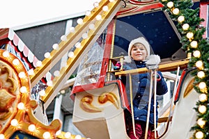 Happy cute preschool girl riding on ferris wheel carousel horse at Christmas funfair or market, outdoors. Little toddler