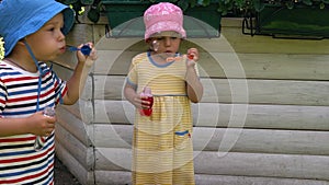 Happy cute preschool simblings children boy and girl blow soap bubbles on hot summer. Kids playing on yard. Baby on park