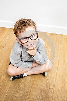 Happy cute schoolboy with serious eyeglasses and tooth missing seated