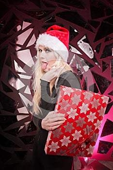 Happy cute slender young woman in christmas fur hat holding gift box on dark nightclub background. bad playful santa