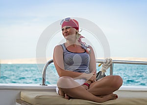 Happy cute sunburnt girl in a red bandana is sitting on a yacht on background of the blue sky and blue sea