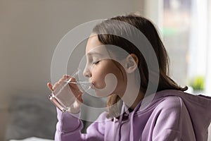 Happy cute thirsty little teen girl drinking glass of fresh pure water.