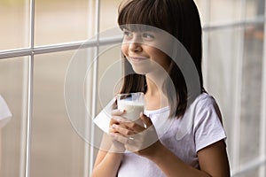 Happy cute thoughtful girl drinking milk, holding glass