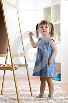 Happy cute toddler girl drawing or writting with marker pen on a blank whiteboard at home, preschool, daycare or