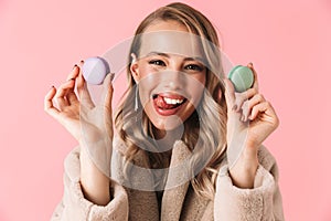 Happy cute young pretty woman posing isolated over pink wall background holding cake macaroons sweeties