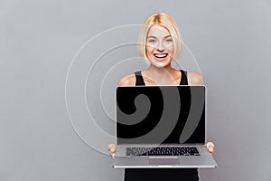 Happy cute young woman holding blank screen laptop