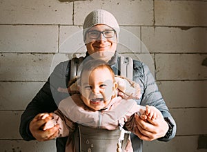 Happy dad and baby in carrier in new house on renovation stage, background of foam concrete, new home