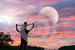 Happy Dad carrying son on shoulders looking future project with the Moon. Silhouette of father and son