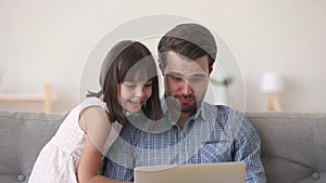 Happy dad and cute child daughter watching cartoons on laptop