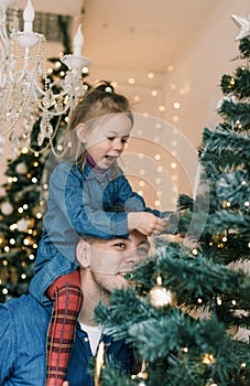 Happy dad and daughter decorate the Christmas tree. Little girl sitting on daddy& x27;s shoulders, close-up