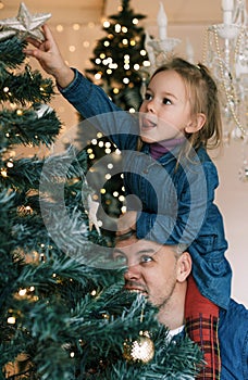 Happy dad and daughter decorate the Christmas tree. Little girl sitting on daddy& x27;s shoulders, close-up