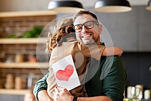 Happy dad getting congratulations from his cute daughter on Fathers day, holding greeting postcard