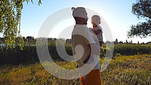 Happy dad holding in hands his son with blonde hair at park on a sunny day. Young father and his little child spending