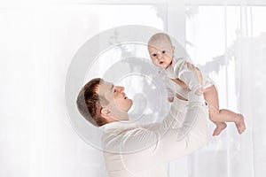Happy dad holding newborn baby at home by the window, happy loving family concept, father`s day