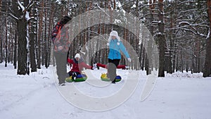 Happy dad and mom pull sleds with children in winter forest. parents play with children in a snowy park in winter. happy