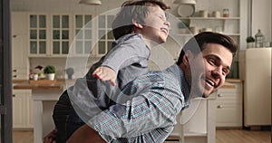 Happy dad piggybacks little preschool son playing together at home