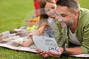 Happy dad receiving handmade postcard from his daughter, father and his little girl having a picnic on a warm day