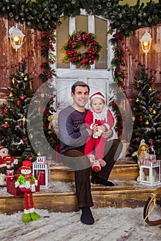 Happy dad in Santa hat play with his little son dressed as Santa Claus on the background of New Year and Christmas interior