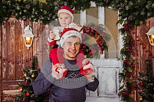 Happy dad in Santa hat play with his little son dressed as Santa Claus on the background of New Year and Christmas interior