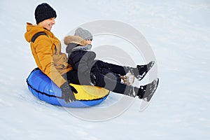 Happy dad and son are sliding from snow hill at tubing.