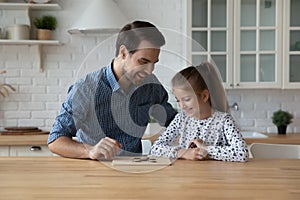 Happy dad teaching daughter kid to play learning board game