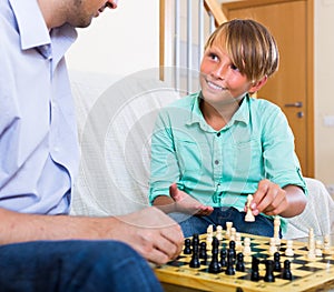 Happy dad and teenage son playing chess