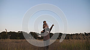 Happy dad walks with cute small daughter sitting on his shoulders through grass field. Young father pointing at