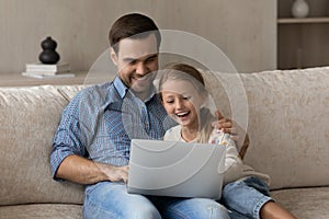 Happy daddy and cheerful daughter kid relaxing on couch