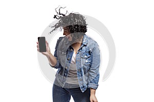 Happy dancing young beautiful girl in jeans shows a smartphone that is emitted on a black screen. Bright brunette with curly hair