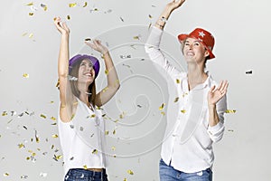 Happy dancing young female friends smiling with confetti against white background. Celebrating