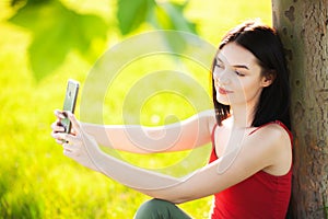 Happy dark brown hair girl with her smartphone under a tree