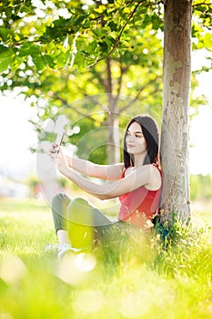 Happy dark brown hair girl with her smartphone under a tree