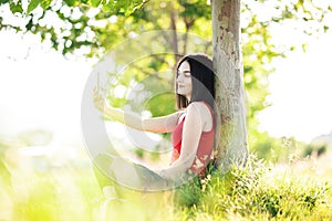 Happy dark brown hair girl with her smartphone under a tree